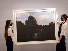 Gallery assistants pose with an artwork entitled 'L'empire des lumieres,1961' by Belgian artist Rene Magritte, during a photocall ahead of a sale of Modern and Contemporary Art, at Sotheby's auction house in London on February 22, 2022.