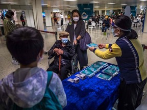 An MTR (Mass Transit Railway) employee hands out a pack of face masks as people leave after receiving the Sinovac COVID-19 coronavirus vaccine at a vaccination centre set up inside a train station in Hong Kong on March 11, 2022.