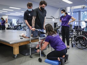 Humboldt Broncos bus crash survivor Ryan Straschnitzki, centre, is helped to stand in a walker by Eric Daigle, left, and Jill Mack, centre right,  while he attends a physiotherapy session in Calgary, June 24, 2021.
