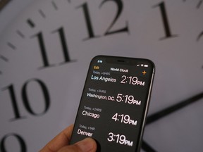 This illustration photo shows a clock in the background of a smartphone showing the time after daylight saving time was implemented in Los Angeles, on March 15, 2022.