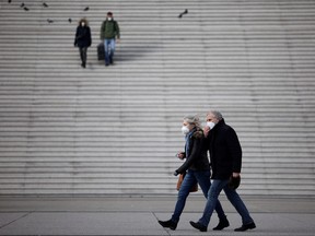 People, wearing protective face masks, walk past the steps near the Grande Arche at the financial and business district of La Defense in Puteaux near Paris, Jan. 31, 2022.