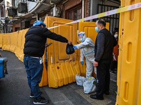 A worker, wearing a protective gear, guards the entrance to a neighborhood in lockdown as a measure against the Covid-19 coronavirus receive food from a delivery man, in Jing'an district, in Shanghai on March 29, 2022.