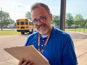 Man in blue shirt holding clipboard with school bus in the background.