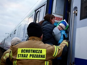 Firefighters help a sick child board a train transformed for medical transport, as 20 children with chronic illnesses and cancer diagnosis came from Kharkiv fleeing the Russian invasion of Ukraine, at the border checkpoint in Medyka, Poland, March 10, 2022.