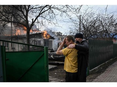 Yevghen Zbormyrsky, 49, is comfirted as he stands in front of his burning home after it was hit by a shelled in the city of Irpin, outside Kyiv, on March 4, 2022.