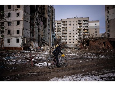 A man rides his bicycle in front of residential buildings damaged in yesterday's shelling in the city of Chernihiv on March 4, 2022.