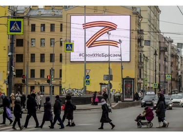 Pedestrians cross a street in front of a billboard displaying the symbol "Z" in the colours of the ribbon of Saint George and a slogan reading: "We don't give up on our people," in support of the Russian armed forces, in St. Petersburg, on March 7, 2022.