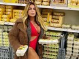 Fit woman wearing red bathing suit under coat holding two cartons of eggs in front of grocery shelves of eggs.