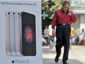 A man speaks on his mobile phone as he walks past an Apple iPhone SE advertisement on a street in New Delhi, India, April 25, 2016.