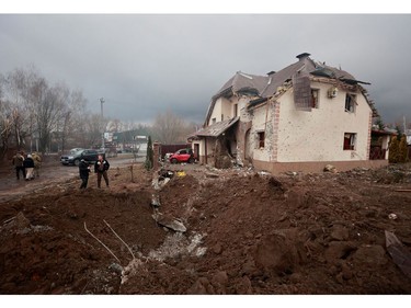 People stand next to a shell crater in front of a house damaged by recent shelling in the village of Hatne, as Russia's invasion of Ukraine continues, in the Kyiv region, March 3, 2022.