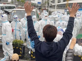 A man raises his hands as a police officer wearing a hazmat suit touches his arm, as residents protest over neighbouring residential compounds being turned into COVID-19 isolation facilities, in Pudong, Shanghai, in this screen grab from a video reported to be April 14, 2022 and obtained by Reuters on April 15, 2022.