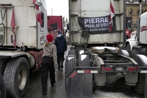 People walk past a truck bearing a flag calling for Conservative MP Pierre Poilievre to become prime minister, on the 20th day of a protest against COVID-19 measures in Ottawa, on Wednesday, Feb. 16, 2022.