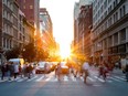 Crowds of busy people walking through the intersection of 5th Avenue and 23rd Street in Manhattan, New York City with bright sunset background.