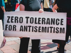 The phrase " Zero tolerance for antisemitism " drawn on a carton banner in hand. A girl holds a cardboard with an inscription. Girls on the street. Protest, march. Rally.