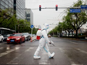 A worker wearing a protective suit and carrying disinfection equipment crosses a road amid the coronavirus disease (COVID-19) outbreak in Beijing, China April 27, 2022.
