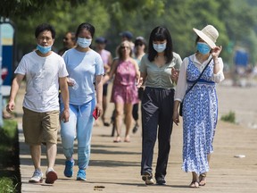People wearing masks walk along the boardwalk in The Beaches neighbourhood in Toronto on Sunday July 25, 2021.