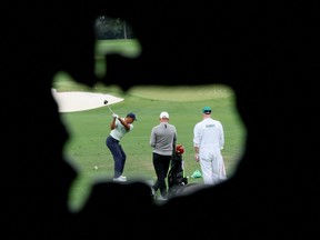 Tiger Woods is seen through the logo of the Augusta National Golf Club hitting a shot on the practice tee.