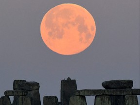 Sheep graze as the full moon, known as the "Super Pink Moon", sets behind Stonehenge stone circle near Amesbury, Britain, April 27, 2021.