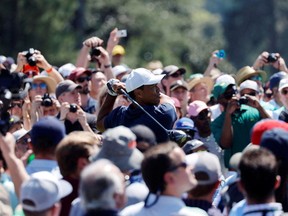 Tiger Woods is surrounded by fans as he hits his tee shot on the 1st during a practice round for the Masters at Augusta National on Monday.