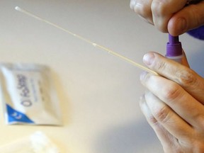 A person holds a swab while sealing a container of testing solution during a rapid antigen test for COVID-19 on  Feb. 25, 2022.