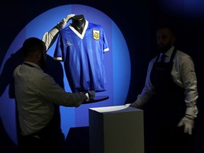In this file photo taken on April 20, 2022 Sotheby's technicians adjust a shirt worn by Argentina's Diego Maradona during the 1986 World Cup quarterfinal match against England, during a photocall at Sotheby's auction house in London ahead of its sale.
