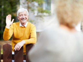 Cheerful and friendly mature man waving hand to his neighbour while standing by fence