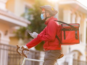 Delivery man wearing face protective mask looking at phone to find the customer address