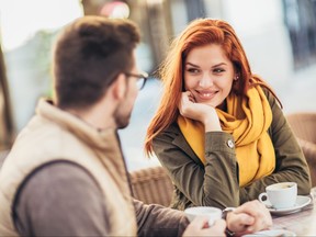 Young couple sitting at the cafe table outdoors, drinking coffee, woman smiling at man adoringly.