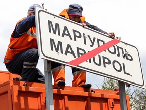 Dieses Handout-Bild, das am 5. Mai 2022 vom Verkehrsministerium der Volksrepublik Donezk aufgenommen und veröffentlicht wurde, zeigt Gemeindeangestellte, die außerhalb der Stadt Mariupol ukrainische Straßenschilder auf Russisch umstellen.