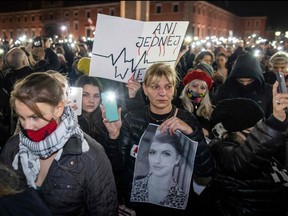 Protesters hold up lights, posters reading "not even one more" and photographs of Iza as they take part in a demonstration on Nov. 6, 2021 in Warsaw, Poland, to mark the first anniversary of a Constitutional Court ruling that imposed a near-total ban on abortion, and also to commemorate the death of pregnant Polish woman Iza.