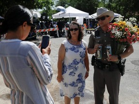 Leti Gomez, left, takes a picture of Angeline Gomez with a Texas Public Safety officer holding flowers they brought to Robb Elementary school, the day after a gunman killed 19 children and two teachers at the school in Uvalde, Texas, Wednesday, May 25, 2022.