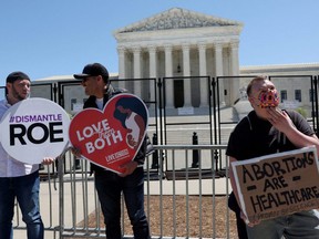 Rene H., right, holds a sign in support of abortion rights as Mark Lee Dickson, of Texas, left, and Mauricio L., of California, hold anti-abortion signs outside the U.S. Supreme Court building in Washington, D.C., May 9, 2022.