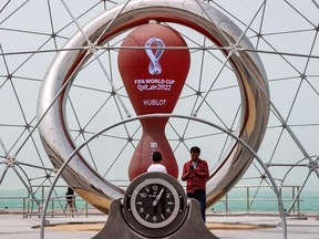 People stand by the clock installation ticking the days to the start of the Qatar 2022 FIFA World Cup, along the waterfront in Qatar's capital Doha during a heavy dust storm on May 17, 2022 as the skyline behind is obscured in the haze.