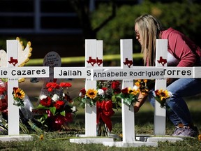A woman lays a flower next to crosses with the names of victims of a school shooting, at a memorial outside Robb Elementary school, two days after a gunman killed nineteen children and two adults, in Uvalde, Texas, U.S. May 26, 2022.