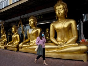 In this file photo taken on January 5, 2021, a woman wearing a face mask walks past golden Buddha statues in Bangkok.