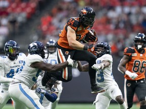 BC Lions' David Mackie tries to jump over the tackle of Argonauts' Shaquille Richardson (bottom) and Sam Acheampong (left) and Robert Priester (second from right) during second half of CFL football action in Vancouver, B.C., Saturday, June 25, 2022.
