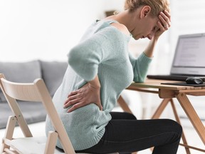 Woman working on a laptop and having headache and back, hip, spine pain.