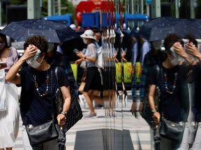 A woman wiping her face is reflected on a window while she walks on a street, as the Japanese government issues a warning over a possible power crunch due to a heatwave in Tokyo, Japan June 28, 2022.