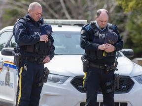 Two RCMP officers observe a moment of silence to honour slain Const. Heidi Stevenson and the other 21 victims of the mass killings at a checkpoint on Portapique Road in Portapique, N.S. on Friday, April 24, 2020.