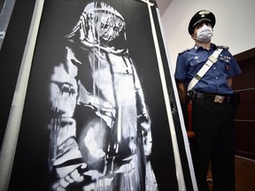In this file photo taken on June 11, 2020 A policeman stands guard near a piece of art attributed to Banksy, that was stolen at the Bataclan in Paris in 2019, and found in Italy, ahead of a press conference in L'Aquila.