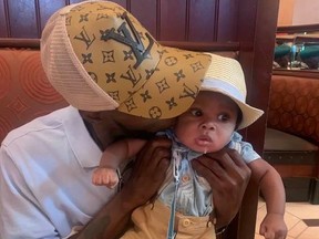 Man, Chase Garrett, whose face is hidden behind hat holding drooling baby. Garrett was fatally shot along with the mother of their son in Connecticut.