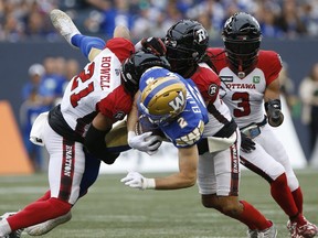 Winnipeg Blue Bombers' Greg Ellingson (2) gets tackled by Ottawa Redblacks' Justin Howell (21) and Sherrod Baltimore (27) during the first half of CFL action in Winnipeg, Friday, June 10, 2022.