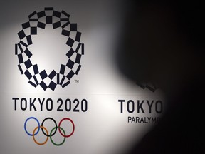 FILE - A person walks near Tokyo 2020 logo in Haneda Airport on June 14, 2021, in Tokyo. Tokyo Olympic officials, meeting Tuesday, June 21, 2022, before the body is dissolved at the end of the month, were to detail the final numbers that were driven up by the pandemic, but were in record range even before that.