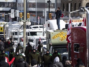 A protester stands on top of his vehicle to watch Surete du Quebec police officers as they surround vehicles in a blockade on Rideau Street, as they aim to end a protest against COVID-19 measures that has grown into a broader anti-government protest, in Ottawa, Feb. 18, 2022.