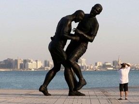 A man takes pictures of a bronze sculpture titled 'Coup de Tete' by Algerian-born French artist Adel Abdessemed during its installation on the Corniche in Doha October 7, 2013. The sculpture, which was bought by the Qatar Museums Authority, was removed on October 28, 2013 after generating criticism from religious conservatives, according to local media. The art work portrays French footballer Zinedine Zidane headbutting Italian player Marco Materazzi during the 2006 World Cup. Picture taken October 7, 2013./File Photo