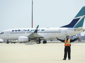 Airline groundcrew work as a grounded Westjest plane sits on the tarmac at Pearson International Airport during the COVID-19 pandemic in Toronto, April 27, 2021.