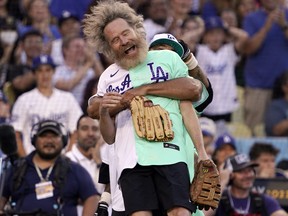 Actor Bryan Cranston is lifted by former Los Angeles Dodgers player Andre Ethier during the MLB All Star Celebrity Softball game, Saturday, July 16, 2022, in Los Angeles.