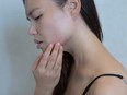 A woman touching her pimples on her cheeks with a worried expression.