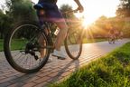 A man rides a bike outdoors in the park on a sunny day at sunset.