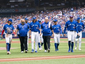 Blue Jays starter Kevin Gausman, third from left, is brought off the field with trainers and players after being hit by a ball in the ankle against the Rays in the second inning of the first game of a doubleheader at the Rogers Centre in Toronto, Saturday, July 2, 2022.